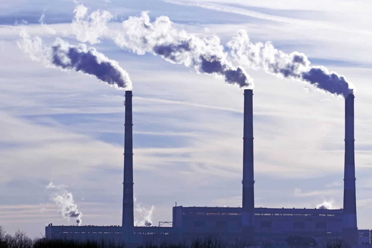 Silhouette van een fabriek met drie rokende schoorstenen